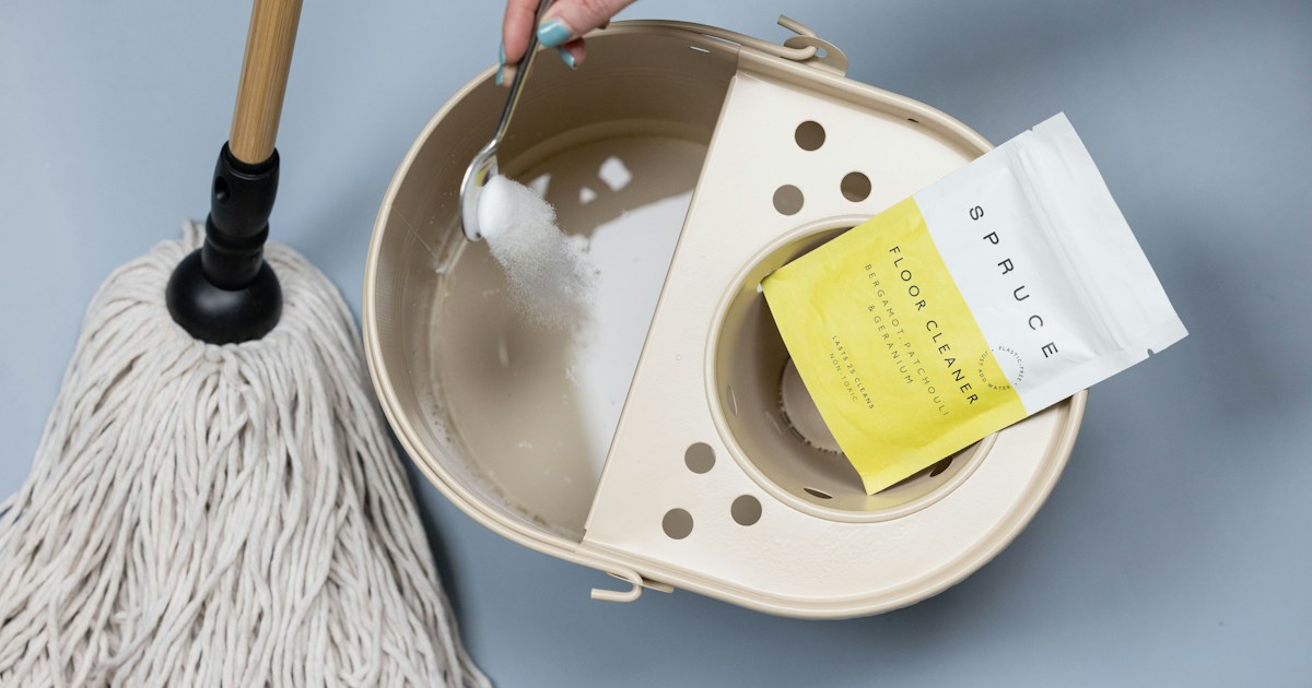 Een hand doseert geconcentreerd schoonmaakpoeder in een dweil emmer, naast de productverpakking